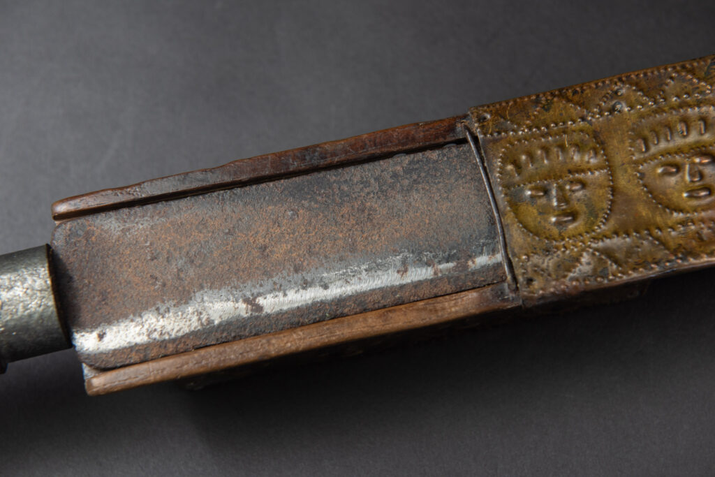 This great sword from the Paiwan tribe is decorated with embossed brass engraved with faces on the front and the side while the back is carved with three characters in the pure Paiwan style.