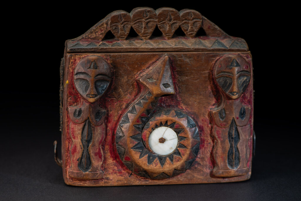Paiwan tribe Shaman box with a sliding lid topped with carved faces, painted with red pigments, featuring full-length figures and the sacred snake, and decorated with mother-of-pearl.