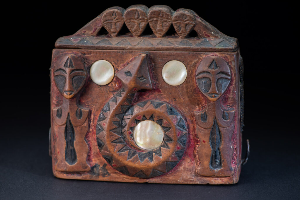 Paiwan tribe Shaman box with a sliding lid topped with carved faces, painted with red pigments, featuring full-length figures and the sacred snake, and decorated with mother-of-pearl.