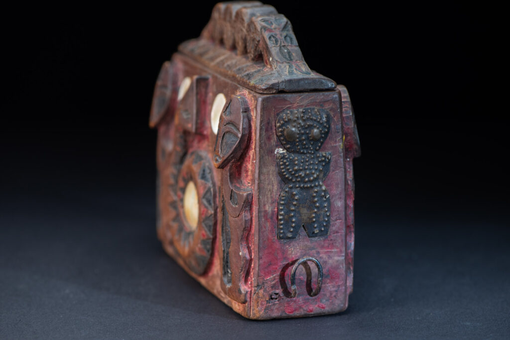 Paiwan tribe Shaman box with a sliding lid topped with carved faces, painted with red pigments, featuring full-length figures and the sacred snake, and decorated with mother-of-pearl.