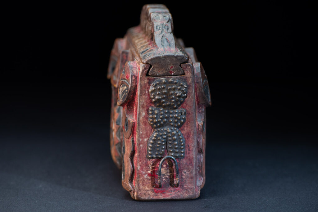Paiwan tribe Shaman box with a sliding lid topped with carved faces, painted with red pigments, featuring full-length figures and the sacred snake, and decorated with mother-of-pearl.