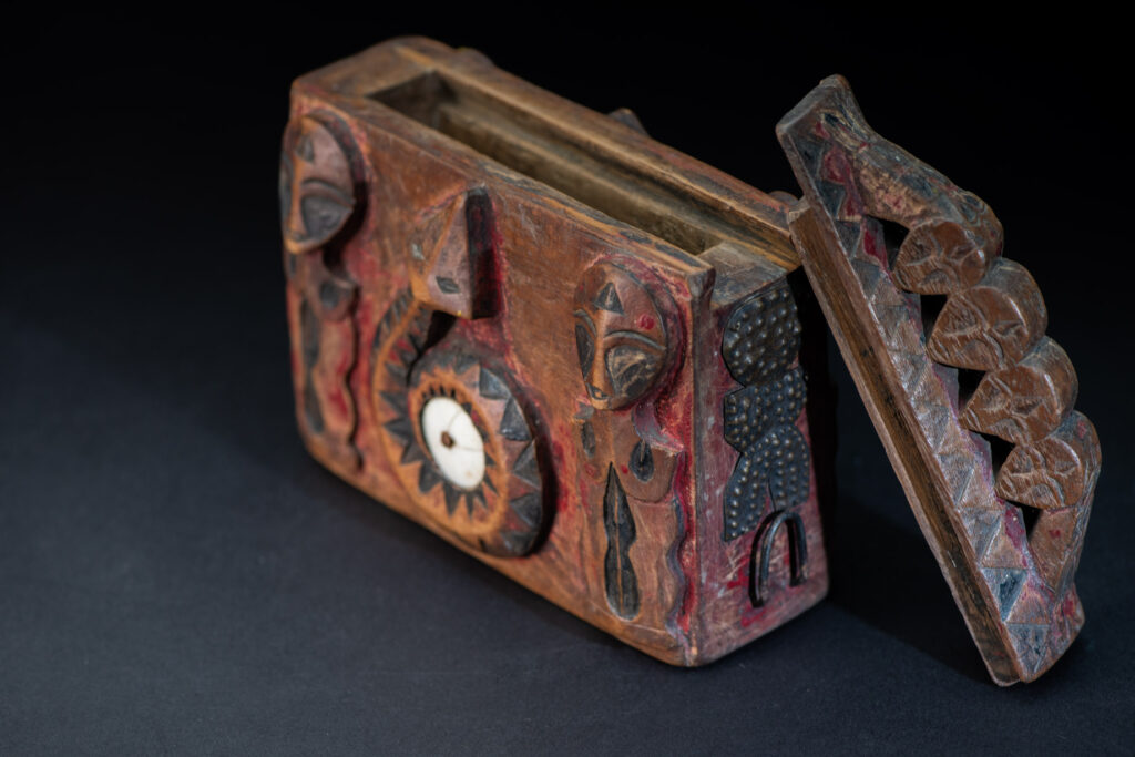 Paiwan tribe Shaman box with a sliding lid topped with carved faces, painted with red pigments, featuring full-length figures and the sacred snake, and decorated with mother-of-pearl.