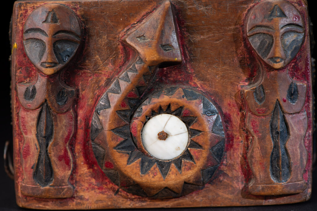 Paiwan tribe Shaman box with a sliding lid topped with carved faces, painted with red pigments, featuring full-length figures and the sacred snake, and decorated with mother-of-pearl.