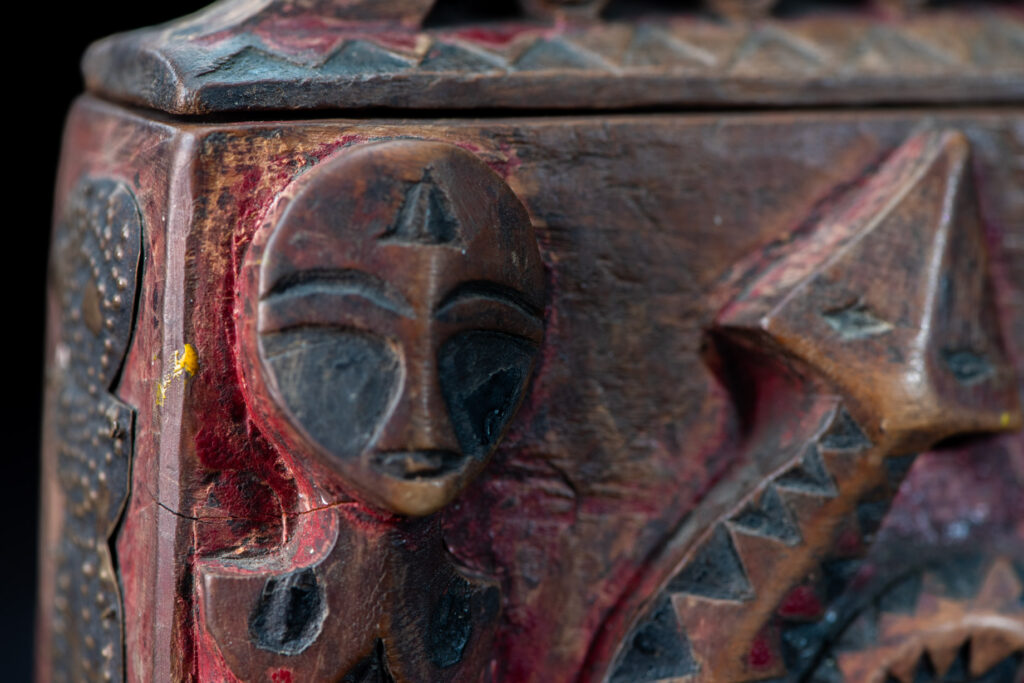 Paiwan tribe Shaman box with a sliding lid topped with carved faces, painted with red pigments, featuring full-length figures and the sacred snake, and decorated with mother-of-pearl.