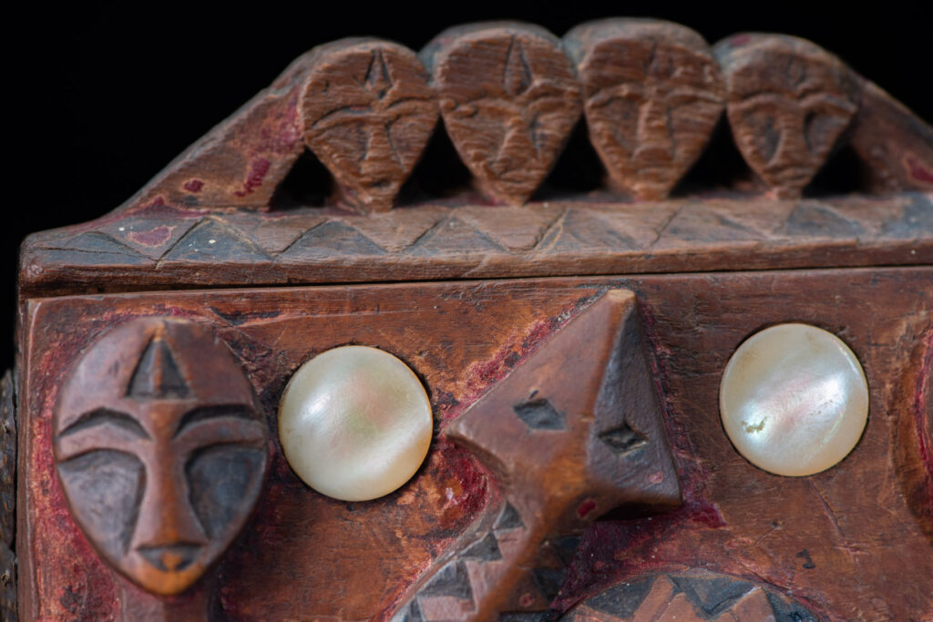 Paiwan tribe Shaman box with a sliding lid topped with carved faces, painted with red pigments, featuring full-length figures and the sacred snake, and decorated with mother-of-pearl.