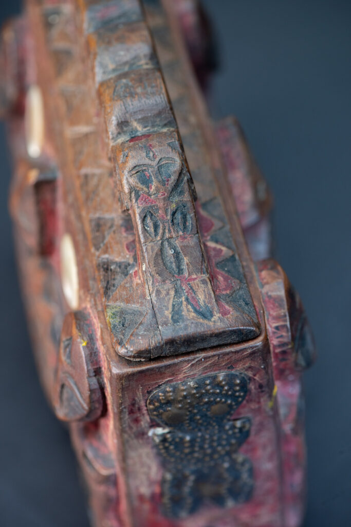 Paiwan tribe Shaman box with a sliding lid topped with carved faces, painted with red pigments, featuring full-length figures and the sacred snake, and decorated with mother-of-pearl.