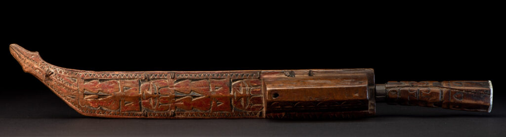 Paiwan tribe hunting knife with a sheath carved with a standing figure and human faces on the side. The hilt is made of carved wood.