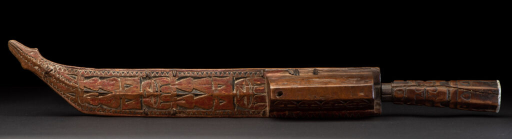Paiwan tribe hunting knife with a sheath carved with a standing figure and human faces on the side. The hilt is made of carved wood.