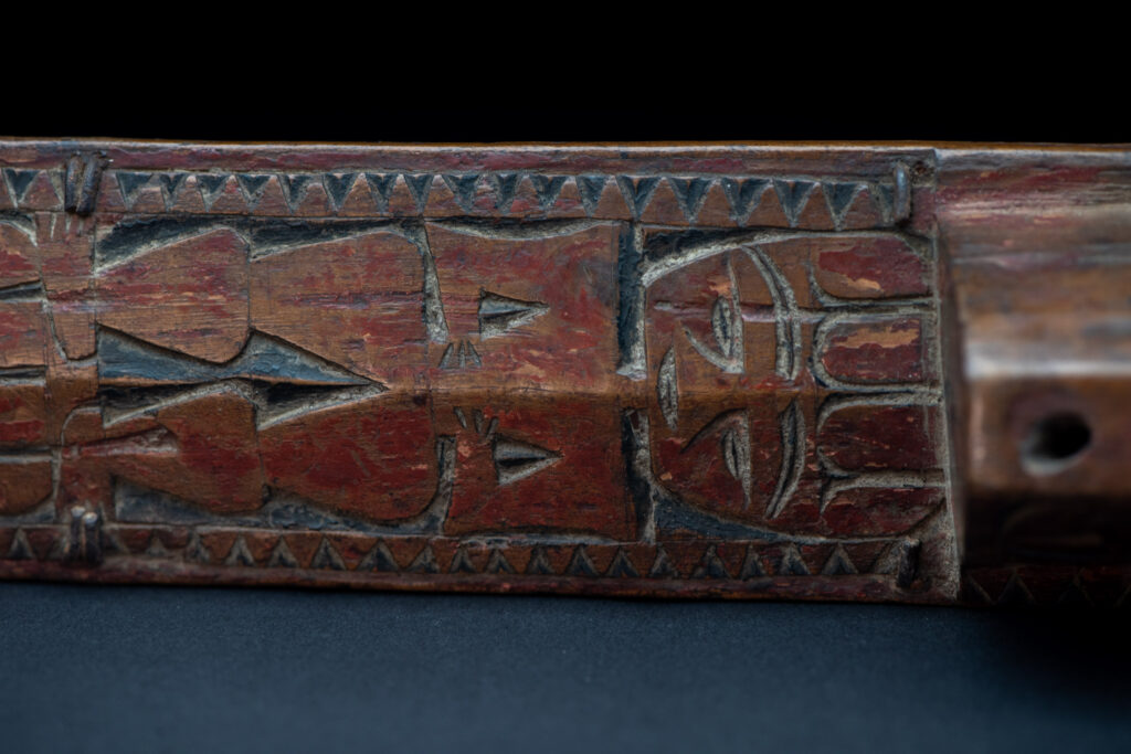 Paiwan tribe hunting knife with a sheath carved with a standing figure and human faces on the side. The hilt is made of carved wood.