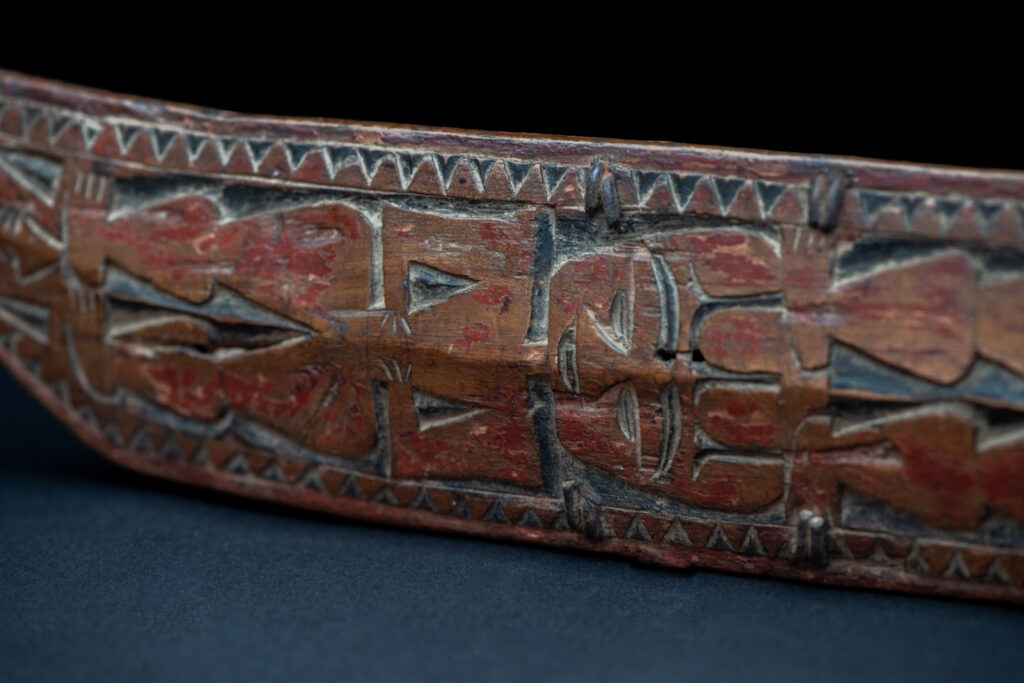 Paiwan tribe hunting knife with a sheath carved with a standing figure and human faces on the side. The hilt is made of carved wood.