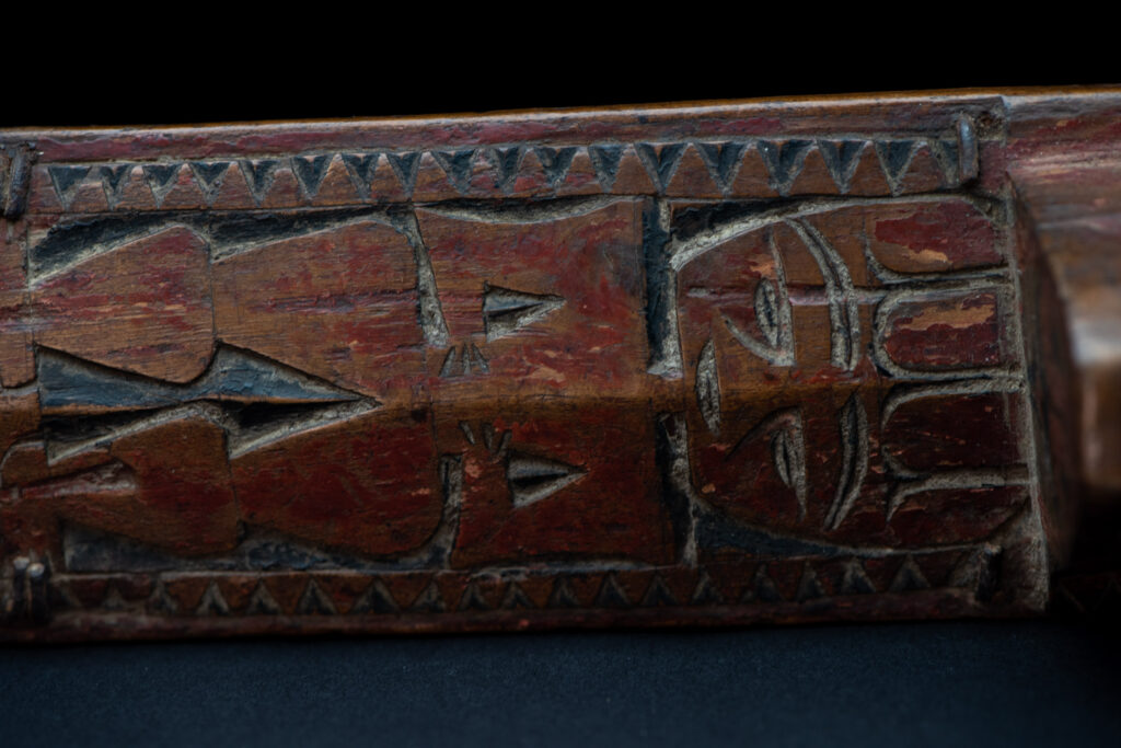 Paiwan tribe hunting knife with a sheath carved with a standing figure and human faces on the side. The hilt is made of carved wood.