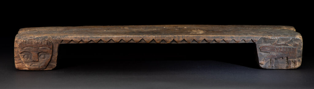 Paiwan tribe headrest in wood carved with human head pattern and deer on both side which represent abundant harvest and performance of ability.