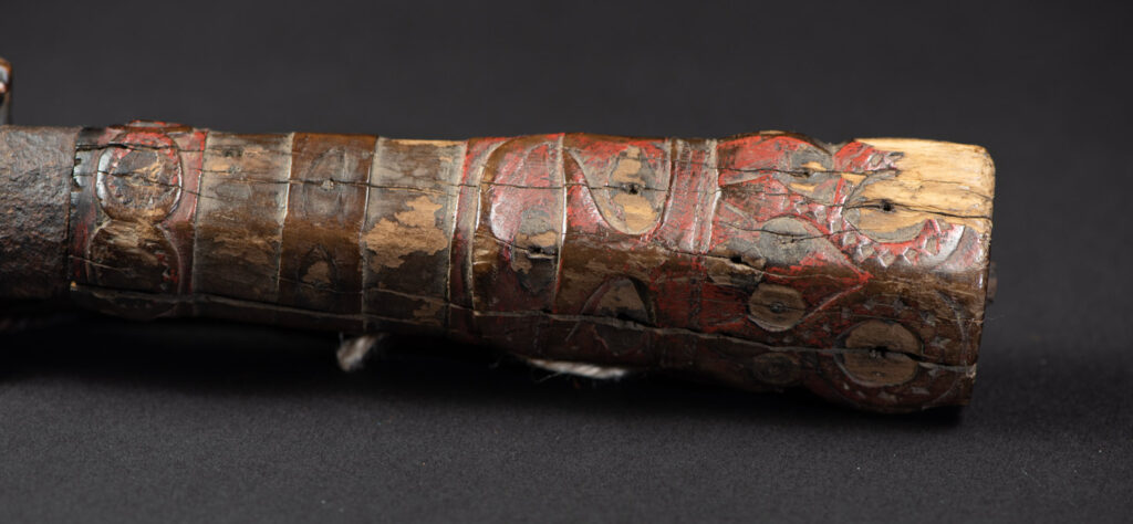 Very fine ceremonial sword from the Paiwan tribe, featuring a sheath carved with full-standing ancestral figures and a handle tinted with red pigment. The sides are carved with human faces.