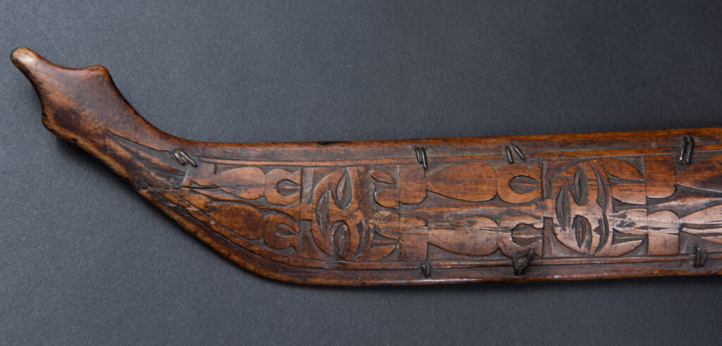 Very fine ceremonial sword from the Paiwan tribe, featuring a sheath carved with full-standing ancestral figures and a handle tinted with red pigment. The sides are carved with human faces.