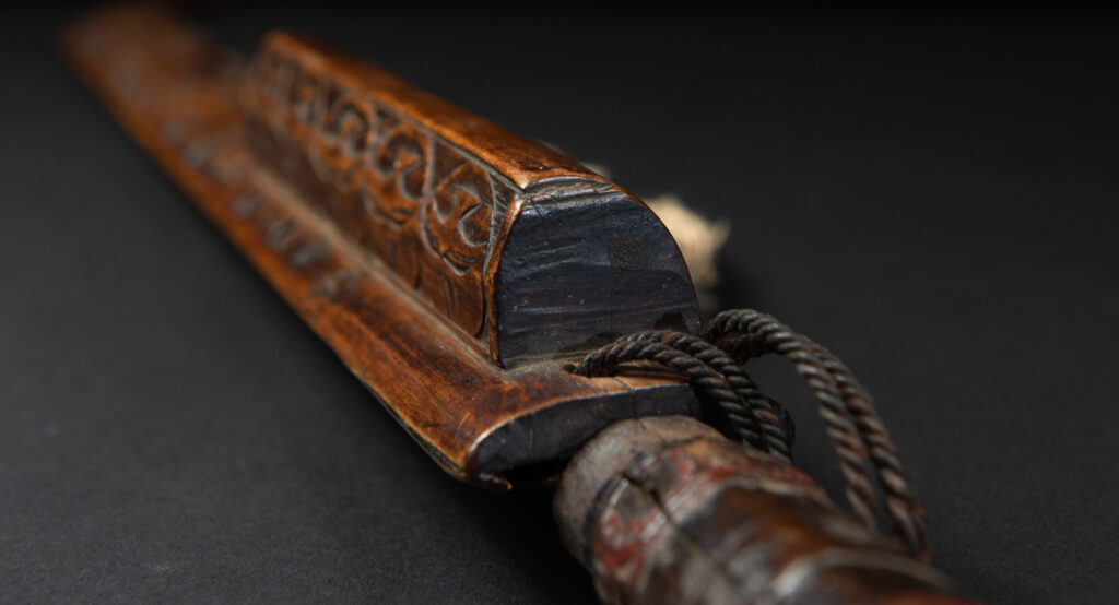 Very fine ceremonial sword from the Paiwan tribe, featuring a sheath carved with full-standing ancestral figures and a handle tinted with red pigment. The sides are carved with human faces.