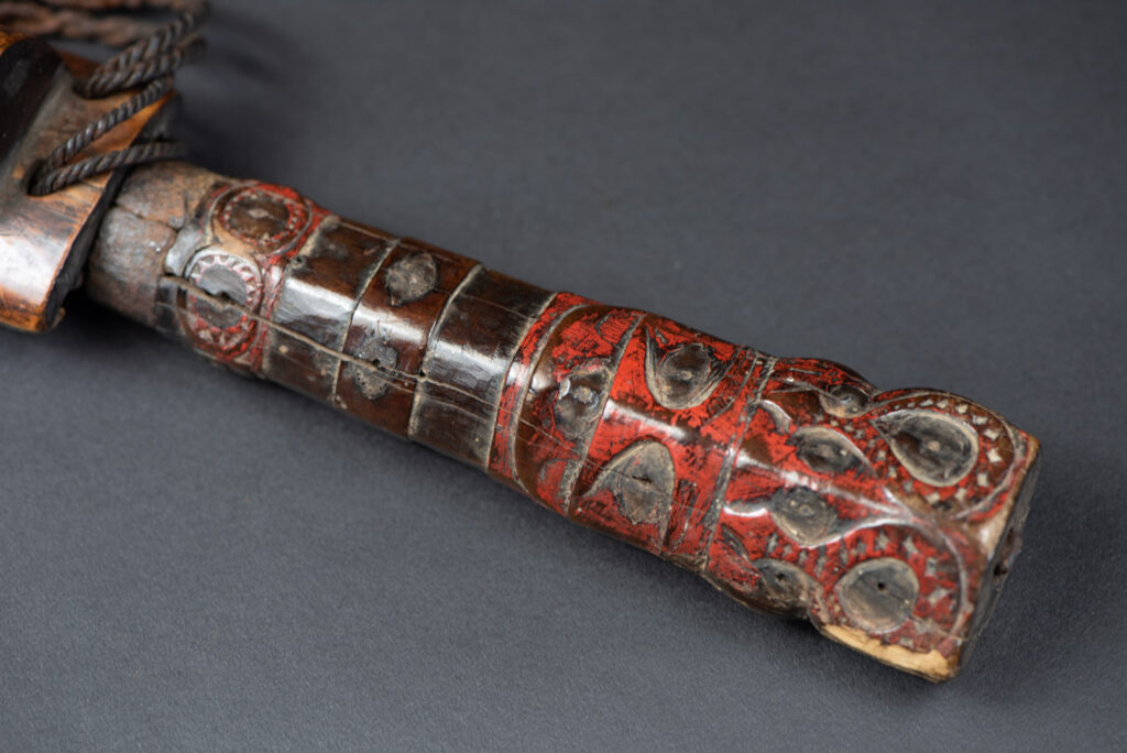 Very fine ceremonial sword from the Paiwan tribe, featuring a sheath carved with full-standing ancestral figures and a handle tinted with red pigment. The sides are carved with human faces.