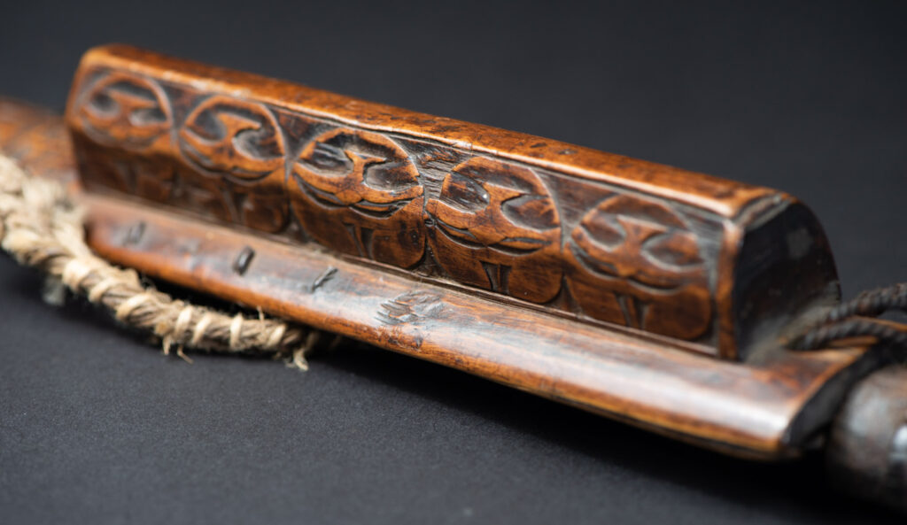 Very fine ceremonial sword from the Paiwan tribe, featuring a sheath carved with full-standing ancestral figures and a handle tinted with red pigment. The sides are carved with human faces.