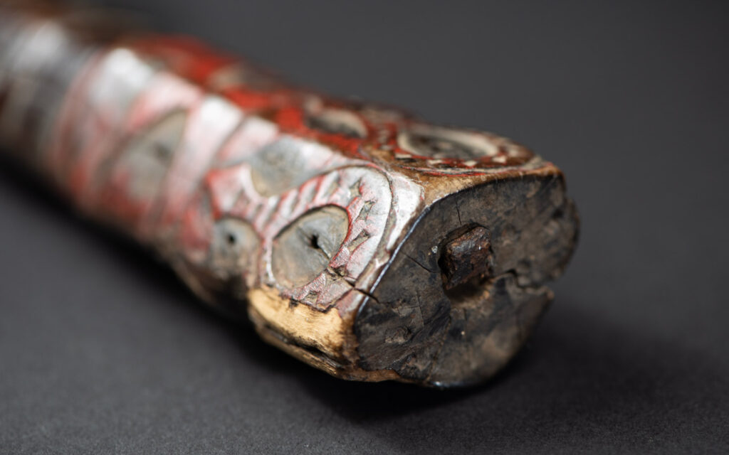 Very fine ceremonial sword from the Paiwan tribe, featuring a sheath carved with full-standing ancestral figures and a handle tinted with red pigment. The sides are carved with human faces.