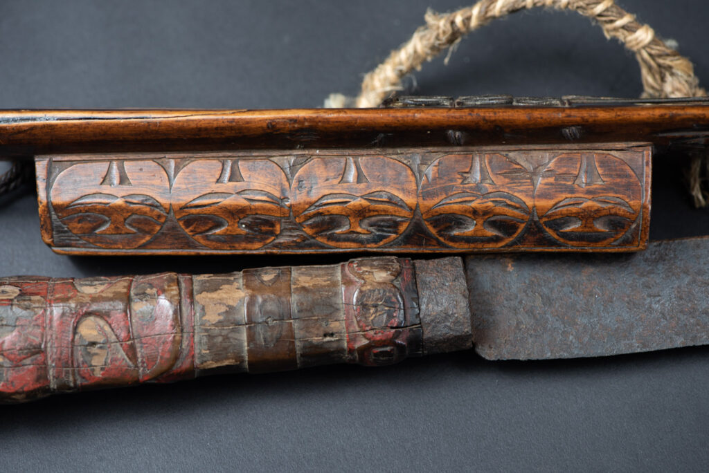Very fine ceremonial sword from the Paiwan tribe, featuring a sheath carved with full-standing ancestral figures and a handle tinted with red pigment. The sides are carved with human faces.