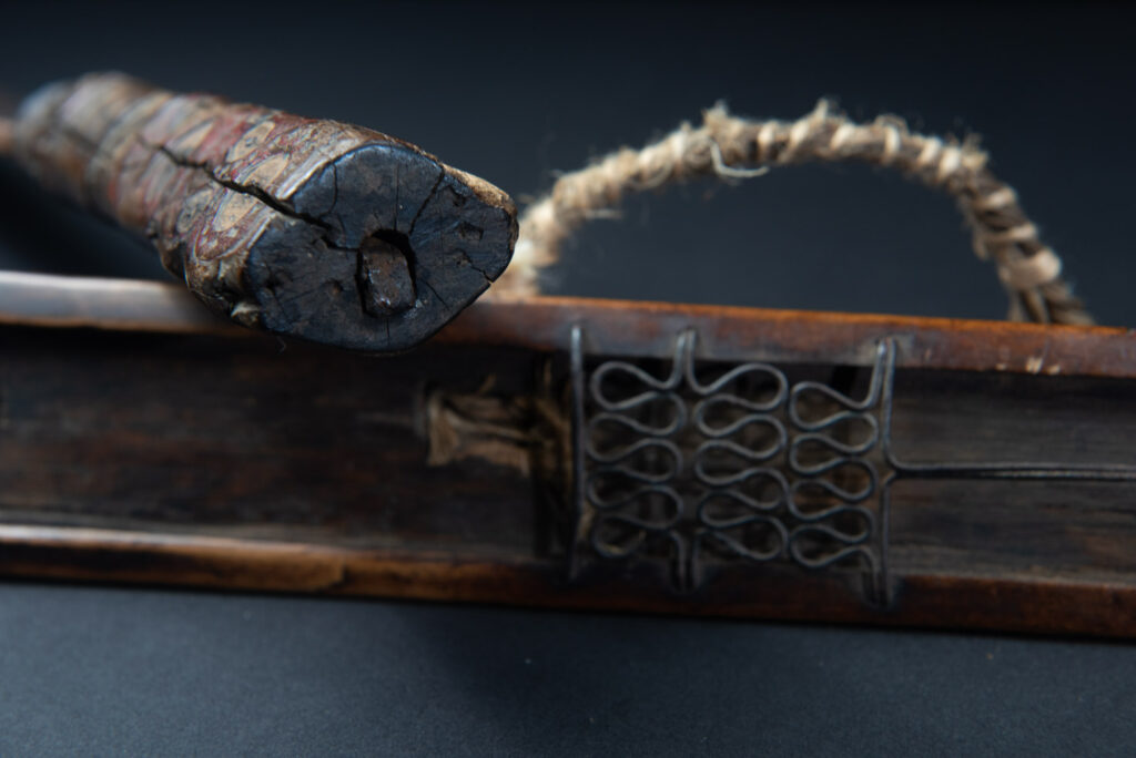 Very fine ceremonial sword from the Paiwan tribe, featuring a sheath carved with full-standing ancestral figures and a handle tinted with red pigment. The sides are carved with human faces.