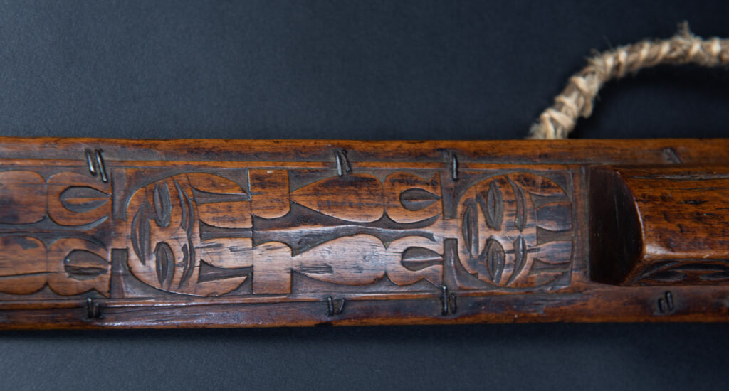 Very fine ceremonial sword from the Paiwan tribe, featuring a sheath carved with full-standing ancestral figures and a handle tinted with red pigment. The sides are carved with human faces.