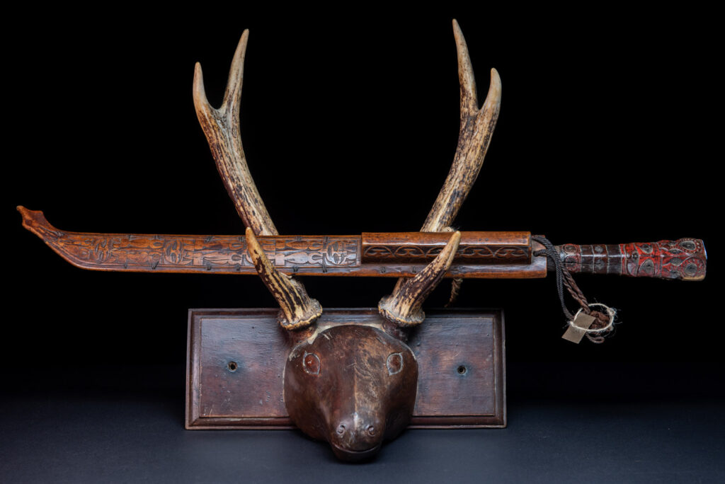 Very fine ceremonial sword from the Paiwan tribe, featuring a sheath carved with full-standing ancestral figures and a handle tinted with red pigment. The sides are carved with human faces.