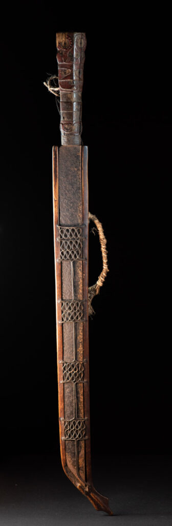 Very fine ceremonial sword from the Paiwan tribe, featuring a sheath carved with full-standing ancestral figures and a handle tinted with red pigment. The sides are carved with human faces.