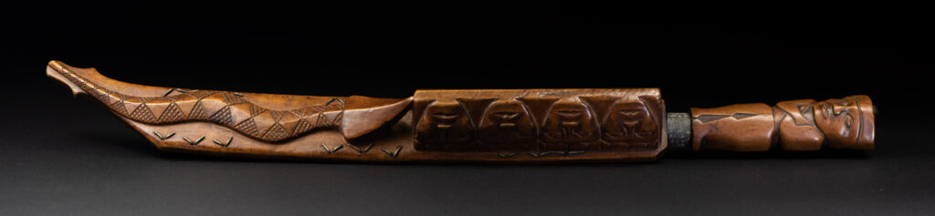 Very fine sword from the Paiwan tribe, carved with the sacred snake and human faces along the sides. The hilt features a full-length standing figure.