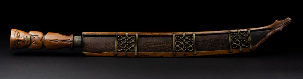 Very fine sword from the Paiwan tribe, carved with the sacred snake and human faces along the sides. The hilt features a full-length standing figure.