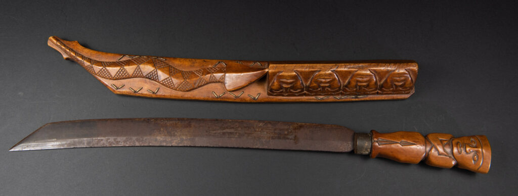Very fine sword from the Paiwan tribe, carved with the sacred snake and human faces along the sides. The hilt features a full-length standing figure.