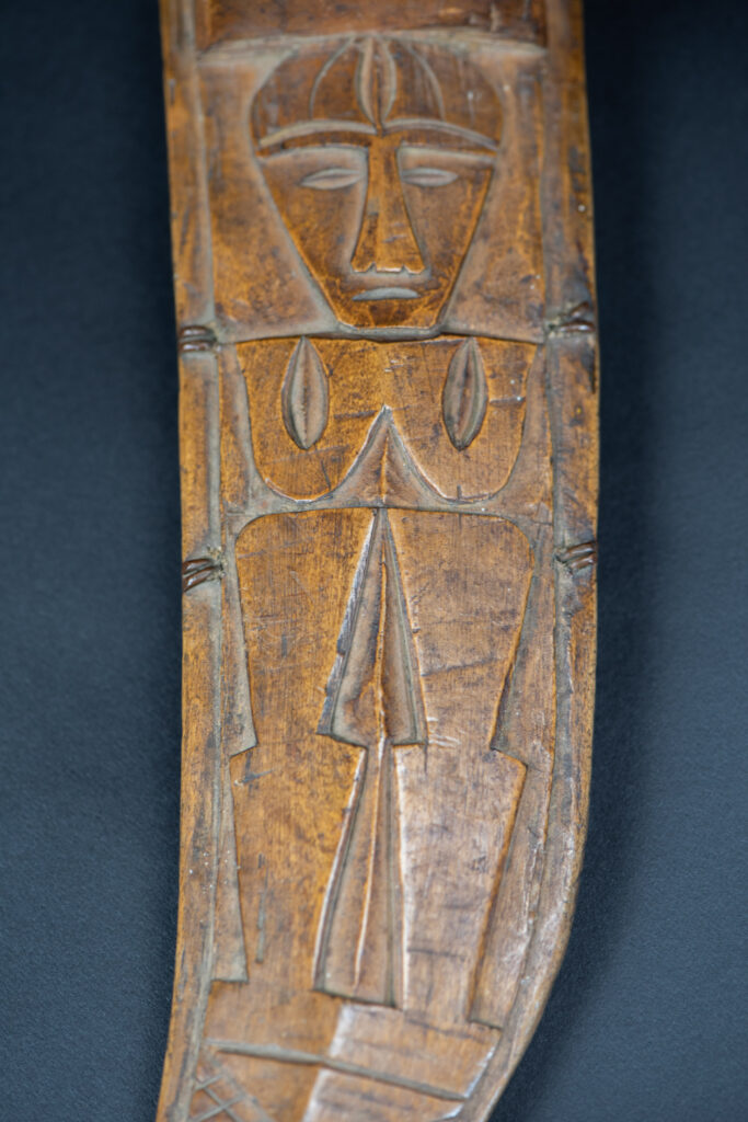 Short sword from the Paiwan tribe, with a sheath carved with a standing figure. The side of the sheath is adorned with three sculpted human heads. The sword is made in one piece with the handle, which is wrapped in rattan.