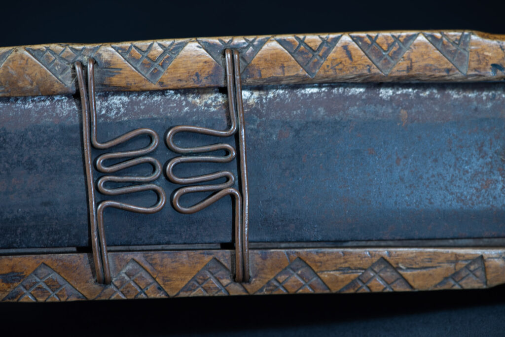 Short sword from the Paiwan tribe, with a sheath carved with a standing figure. The side of the sheath is adorned with three sculpted human heads. The sword is made in one piece with the handle, which is wrapped in rattan.