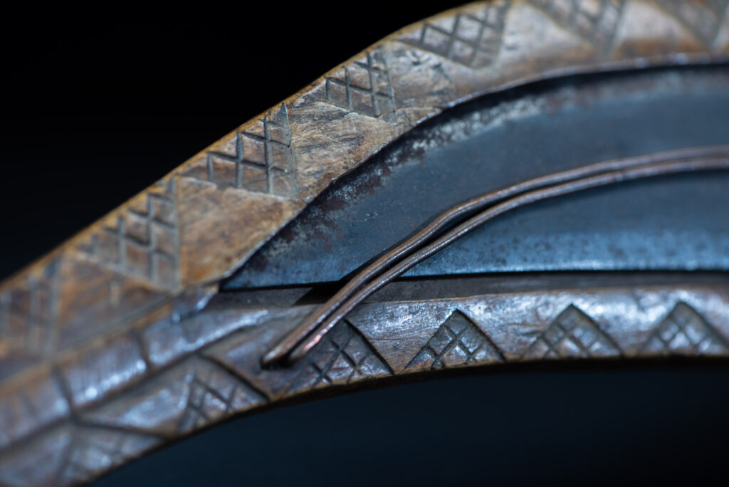 Short sword from the Paiwan tribe, with a sheath carved with a standing figure. The side of the sheath is adorned with three sculpted human heads. The sword is made in one piece with the handle, which is wrapped in rattan.