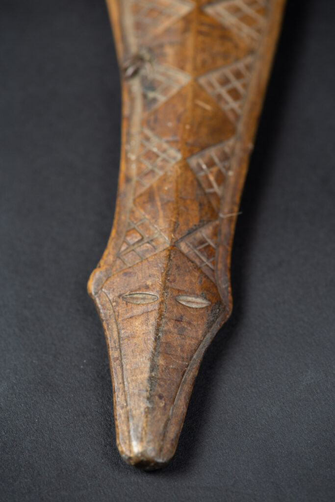 Short sword from the Paiwan tribe, with a sheath carved with a standing figure. The side of the sheath is adorned with three sculpted human heads. The sword is made in one piece with the handle, which is wrapped in rattan.