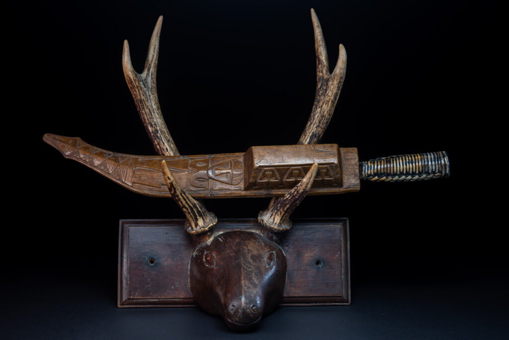 Short sword from the Paiwan tribe, with a sheath carved with a standing figure. The side of the sheath is adorned with three sculpted human heads. The sword is made in one piece with the handle, which is wrapped in rattan.