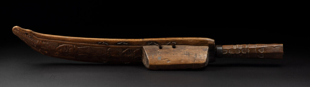 Paiwan tribe hunting knife with a sheath carved with a standing figure and human faces on the side. The hilt is made of carved wood.