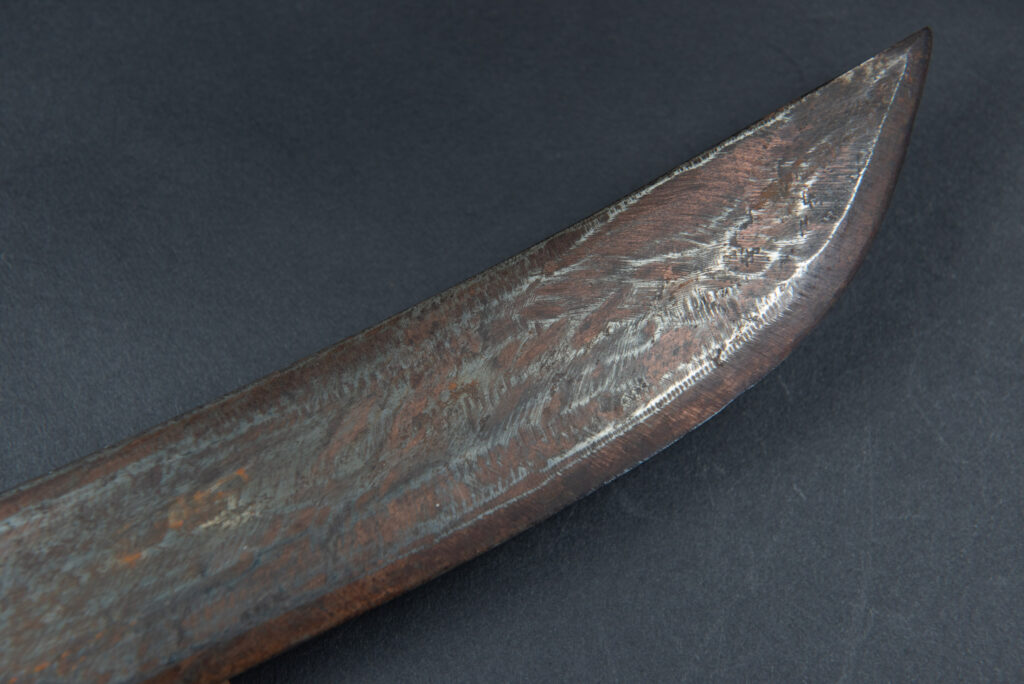 Paiwan tribe hunting knife with a sheath carved with a standing figure and human faces on the side. The hilt is made of carved wood.