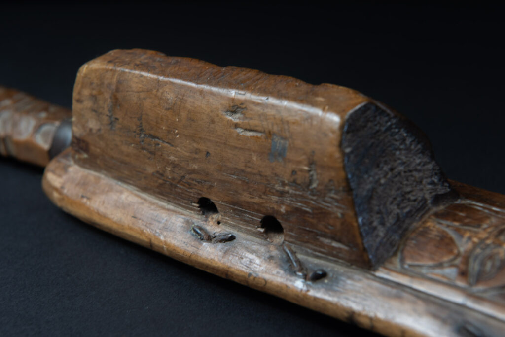 Paiwan tribe hunting knife with a sheath carved with a standing figure and human faces on the side. The hilt is made of carved wood.