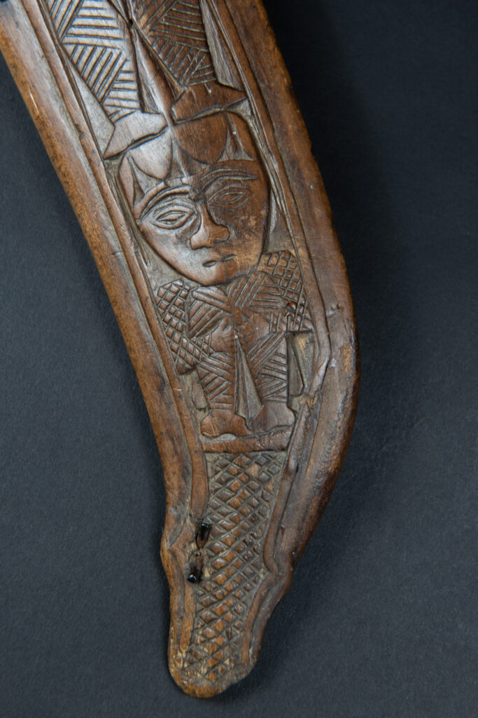 Paiwan tribe hunting knife with a sheath carved with a standing figure and human faces on the side. The hilt is made of carved wood.