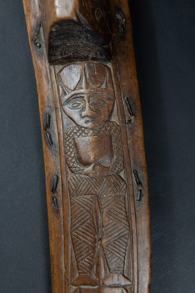 Paiwan tribe hunting knife with a sheath carved with a standing figure and human faces on the side. The hilt is made of carved wood.