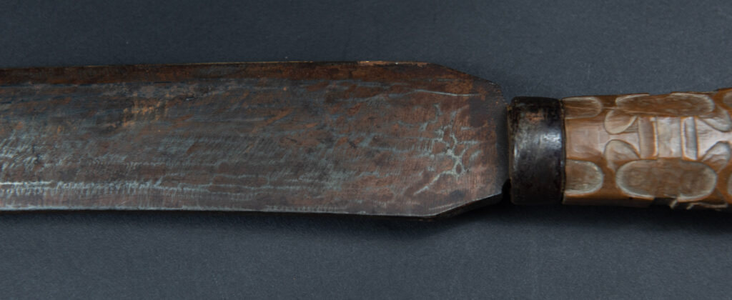 Paiwan tribe hunting knife with a sheath carved with a standing figure and human faces on the side. The hilt is made of carved wood.