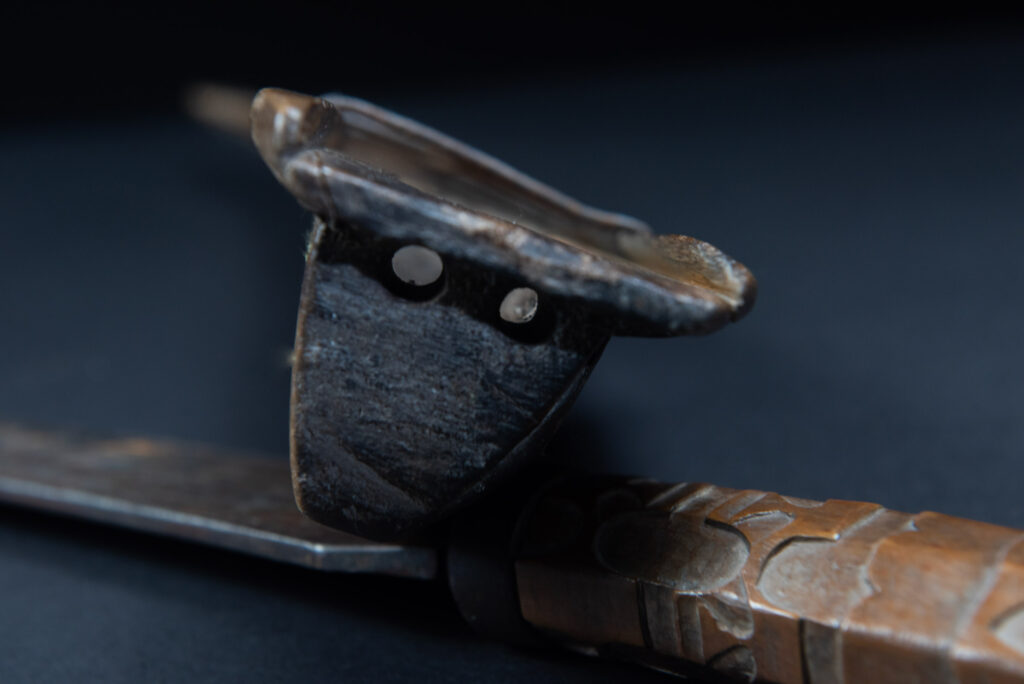 Paiwan tribe hunting knife with a sheath carved with a standing figure and human faces on the side. The hilt is made of carved wood.