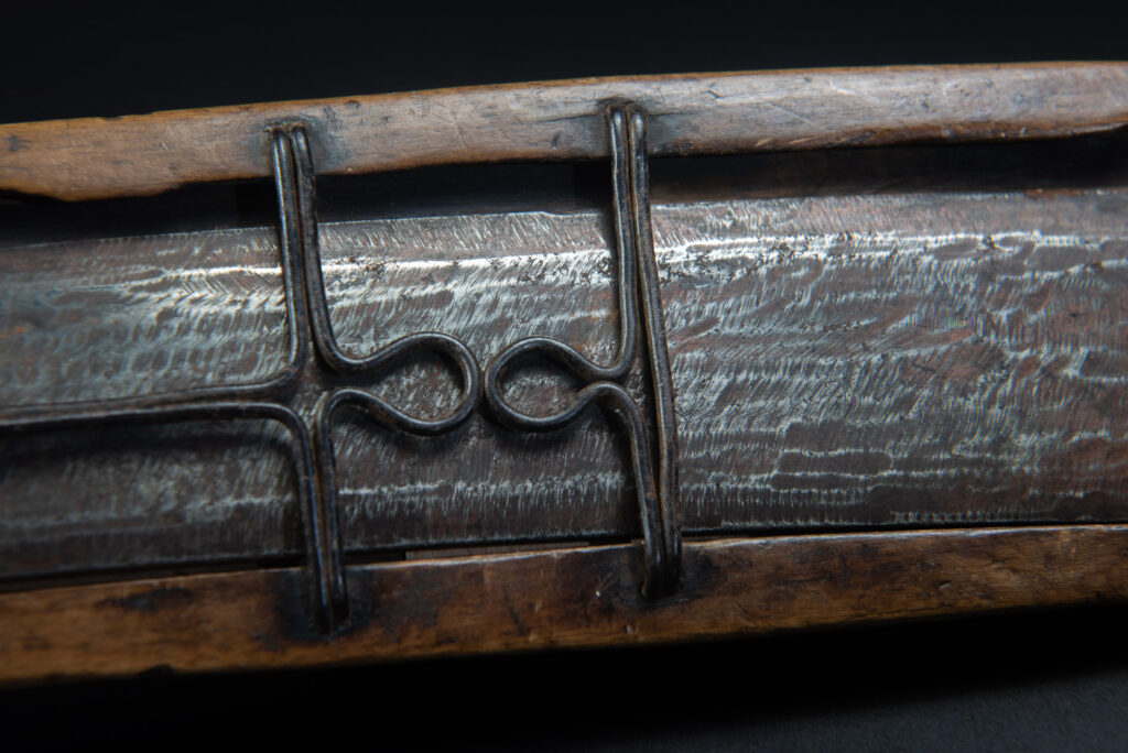 Paiwan tribe hunting knife with a sheath carved with a standing figure and human faces on the side. The hilt is made of carved wood.