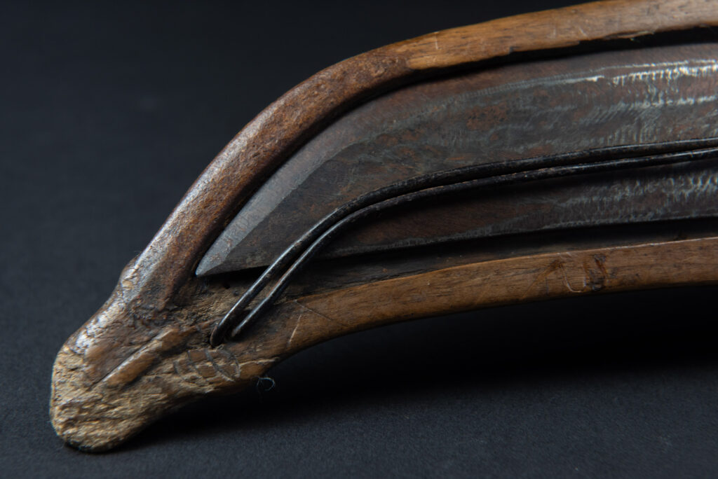 Paiwan tribe hunting knife with a sheath carved with a standing figure and human faces on the side. The hilt is made of carved wood.