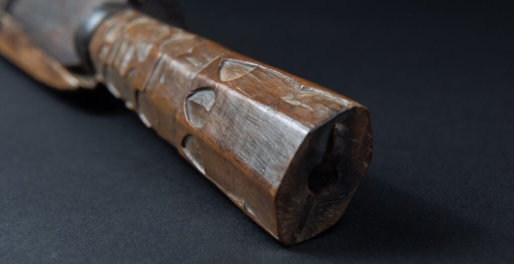 Paiwan tribe hunting knife with a sheath carved with a standing figure and human faces on the side. The hilt is made of carved wood.