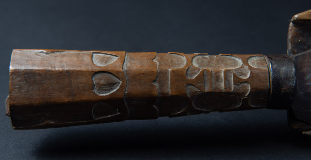 Paiwan tribe hunting knife with a sheath carved with a standing figure and human faces on the side. The hilt is made of carved wood.