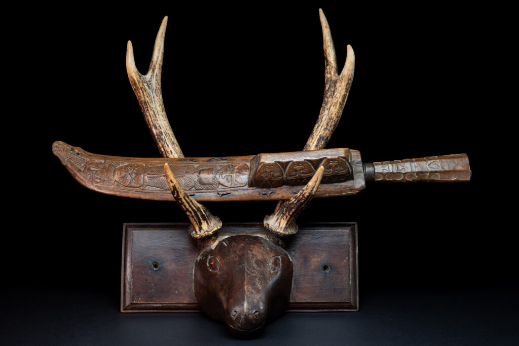 Paiwan tribe hunting knife with a sheath carved with a standing figure and human faces on the side. The hilt is made of carved wood.