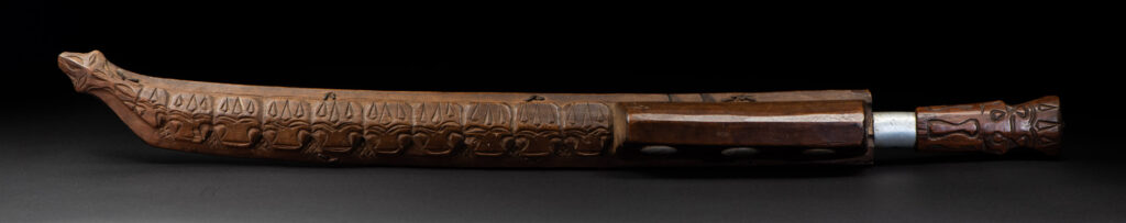 Very fine old sword from the Paiwan tribe, with a scabbard carved with multiple human faces. One side is inlaid with three faience circles.