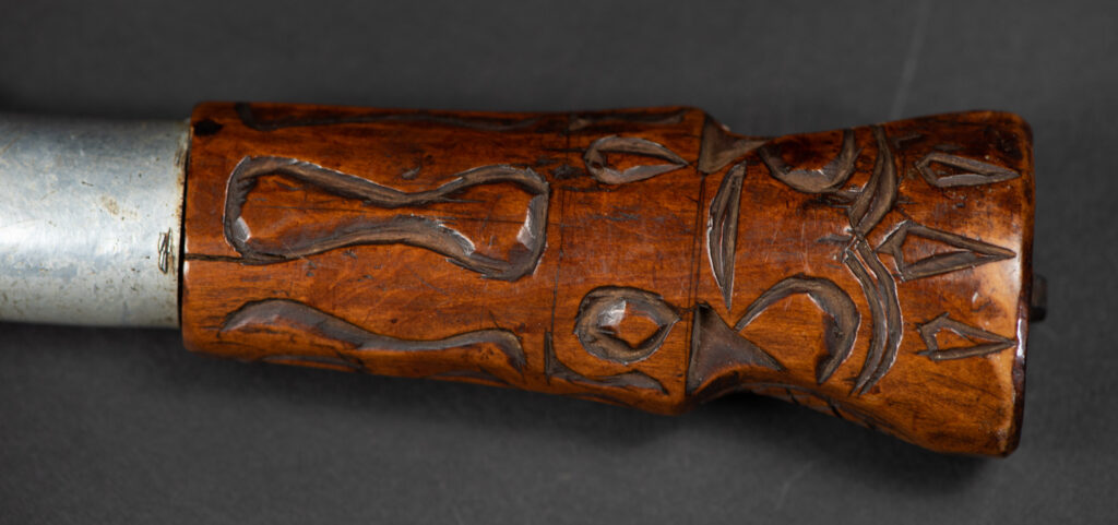 Very fine old sword from the Paiwan tribe, with a scabbard carved with multiple human faces. One side is inlaid with three faience circles.