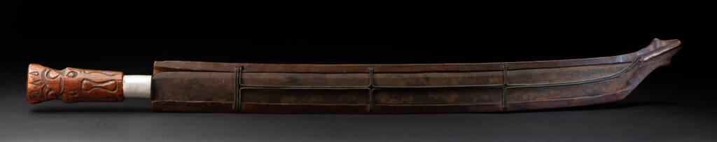 Very fine old sword from the Paiwan tribe, with a scabbard carved with multiple human faces. One side is inlaid with three faience circles.